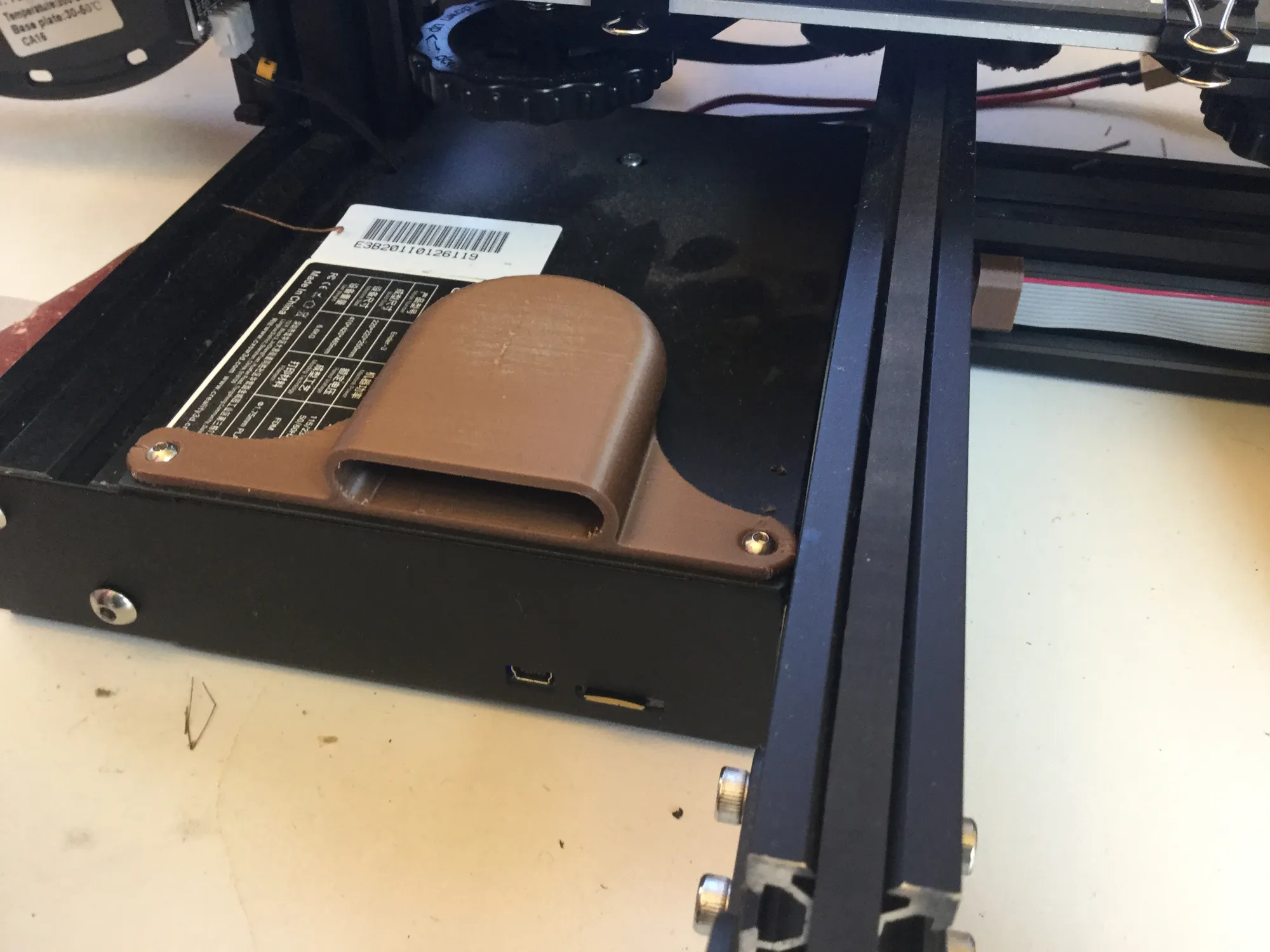 Brown 3D-printed fan duct screwed onto the black mainboard case of a 3D printer, beside aluminum extrusion rails and a ribbon
