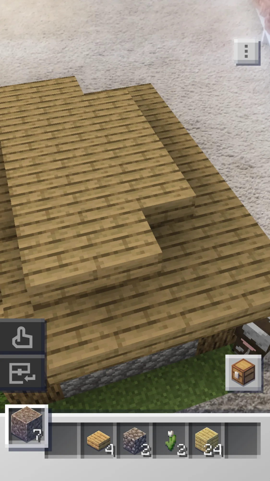 Minecraft Earth AR build of an oak plank roof over cobblestone walls on a carpet, with a cow nearby and an item hotbar below