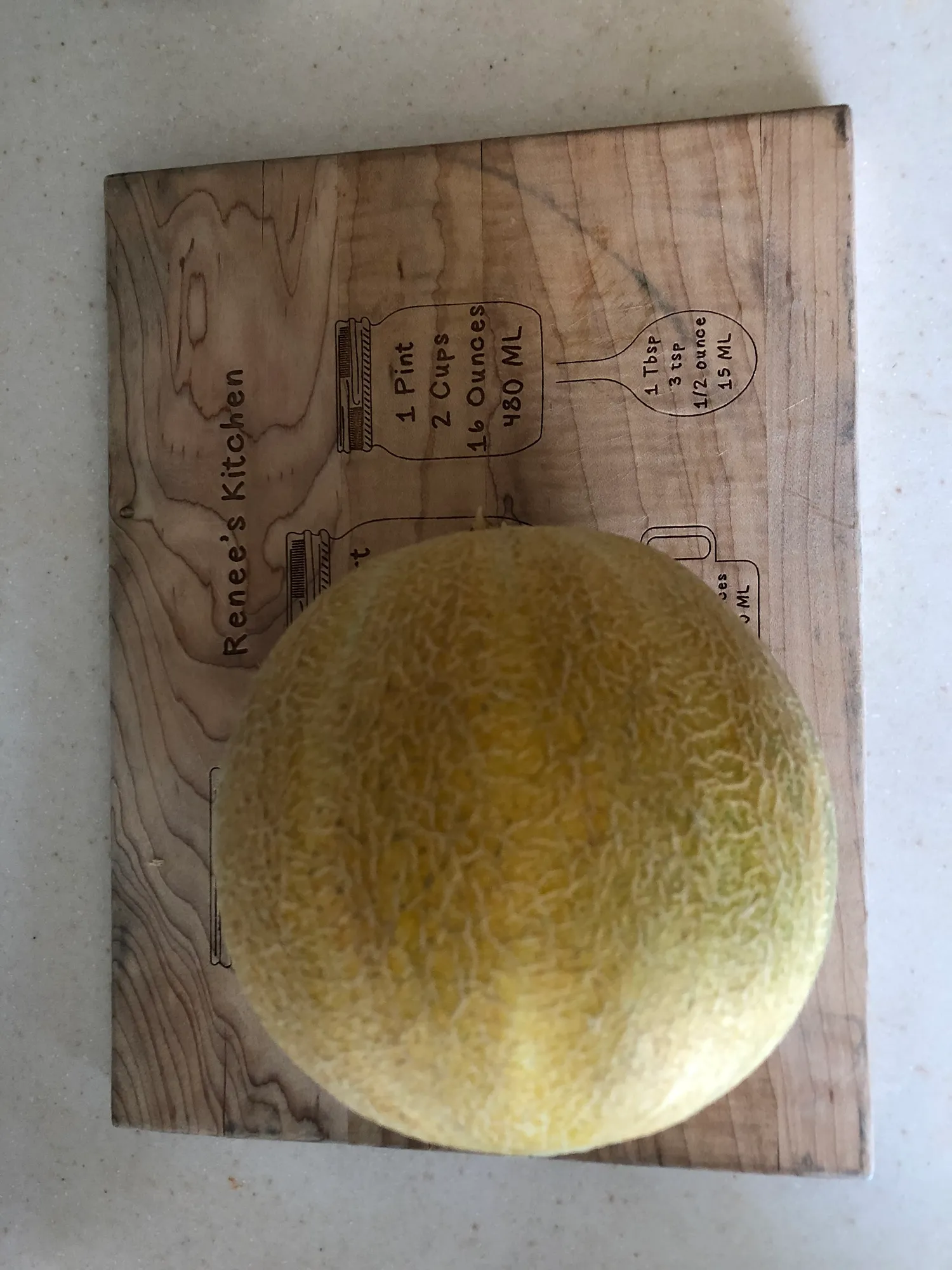 Whole yellow cantaloupe on a wooden cutting board engraved Renee's Kitchen with kitchen measurement conversions