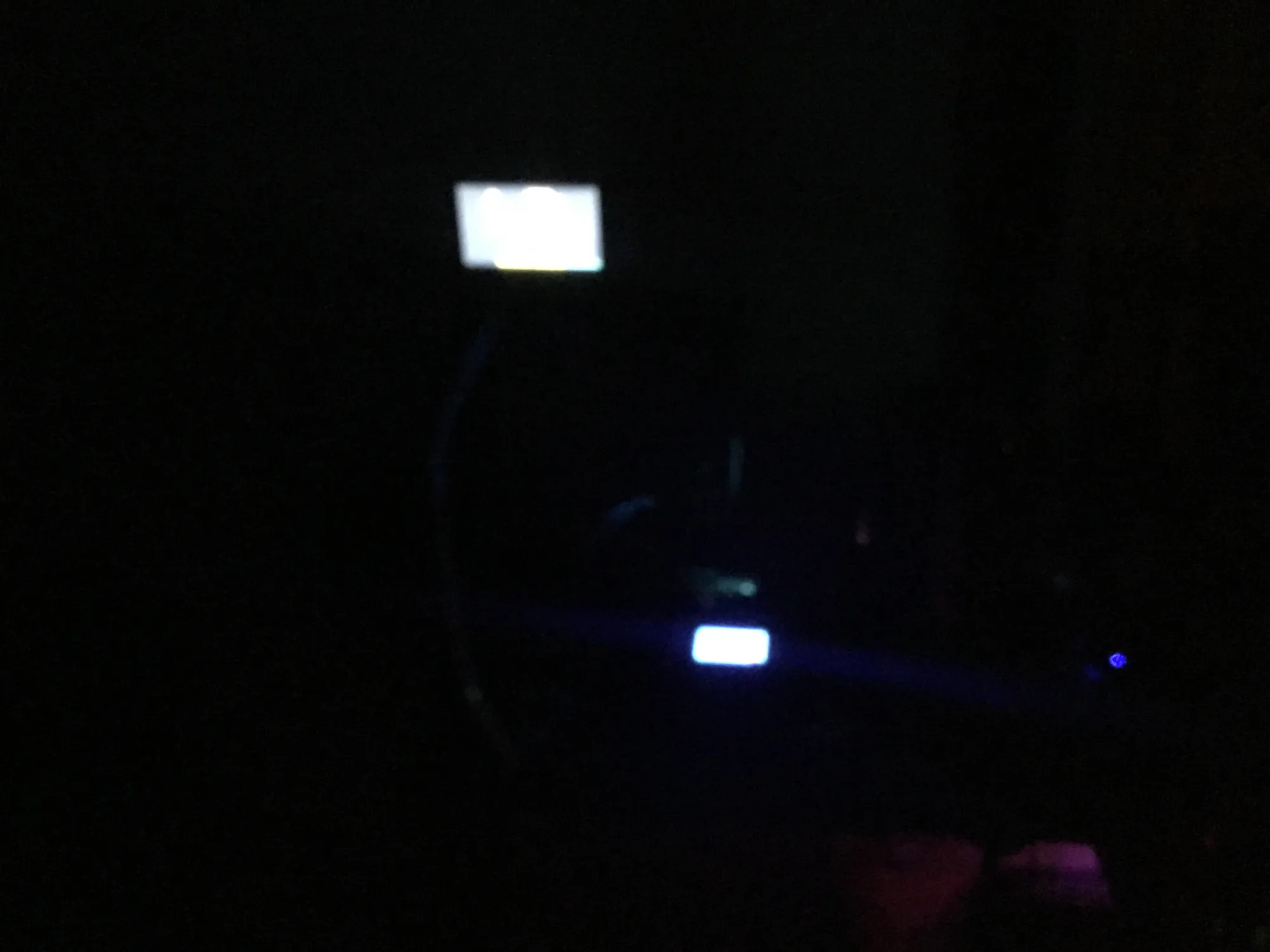 Dark, blurry shot of a 3D printer at night, lit only by a small glowing screen, a blue light strip and faint purple light